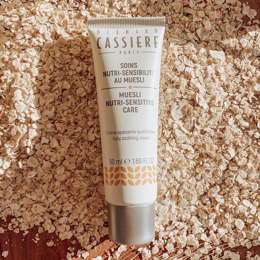 A small bottle of Bernard Cassiere's muesli daily soothing cream laying on a bed of oats.