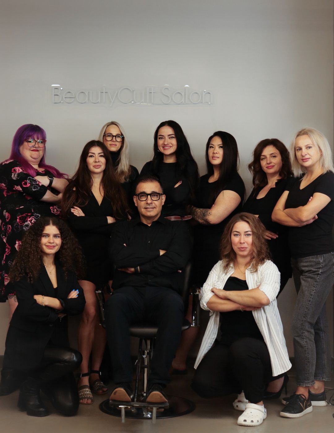 A group of women and one man wearing dark clothing stand together with their arms crossed while in a salon.