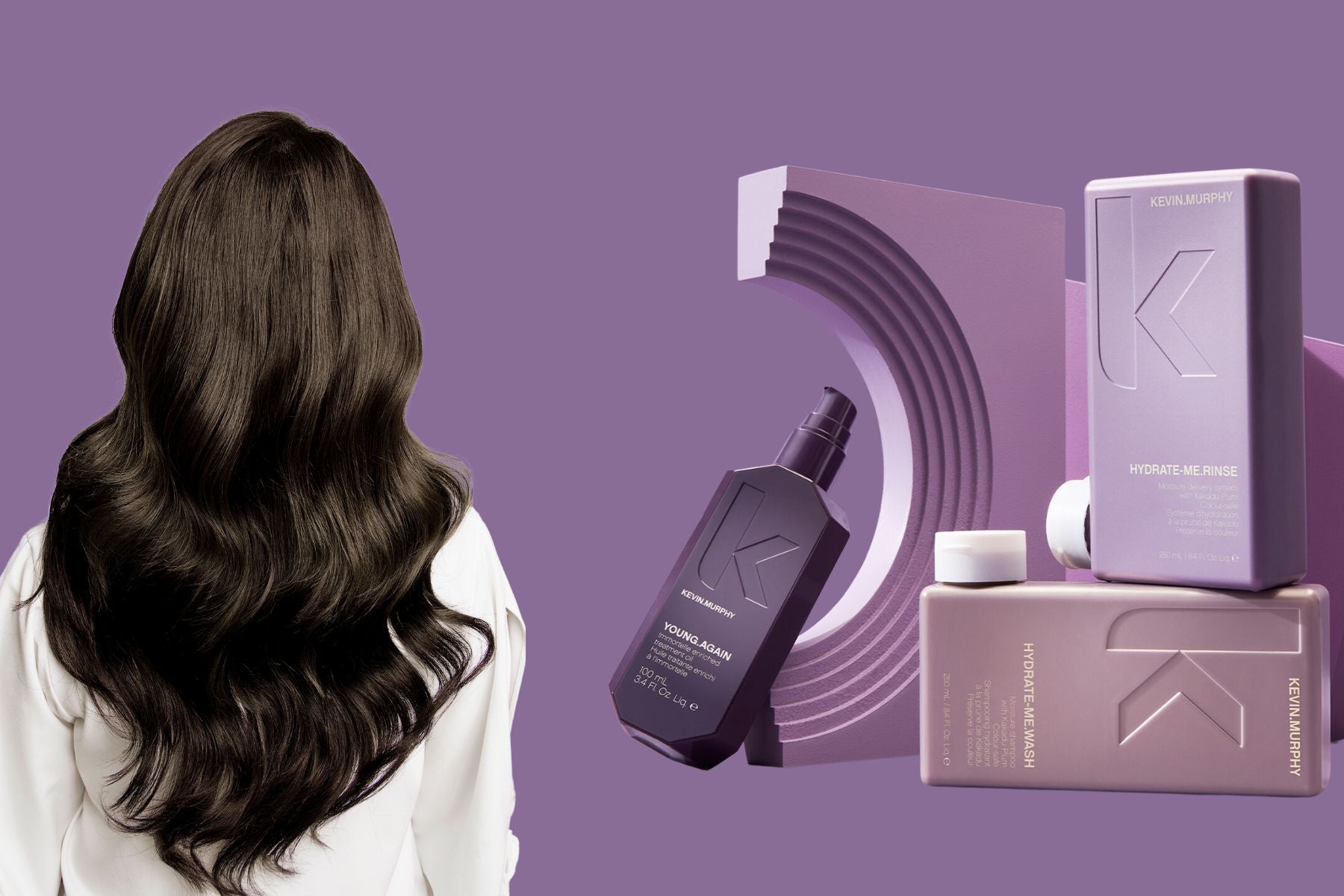 A woman with long, healthy black hair stands beside hair care products from Kevin Murphy's hydration product line.